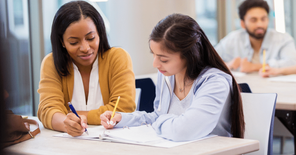 Tutor in public setting with notebook helping student.